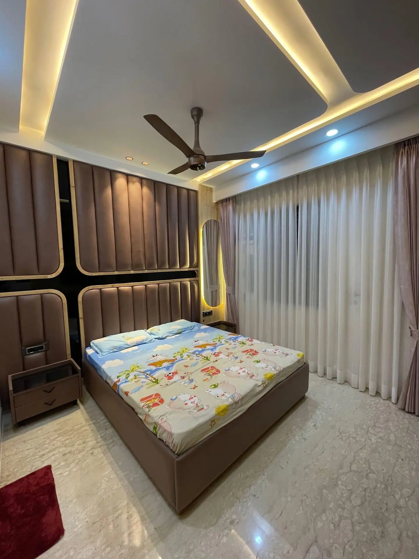 Bedroom with a padded, channel-stitched headboard wall and a layered cove-lit ceiling