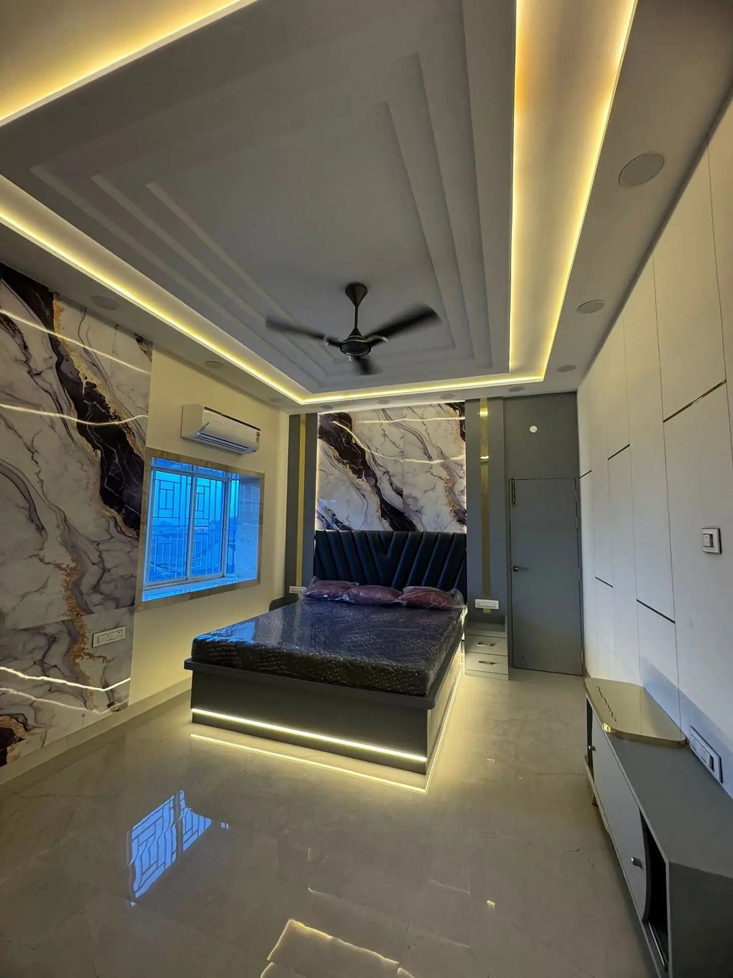 Bedroom with a marble-effect feature wall, stepped cove ceiling and an under-lit bed