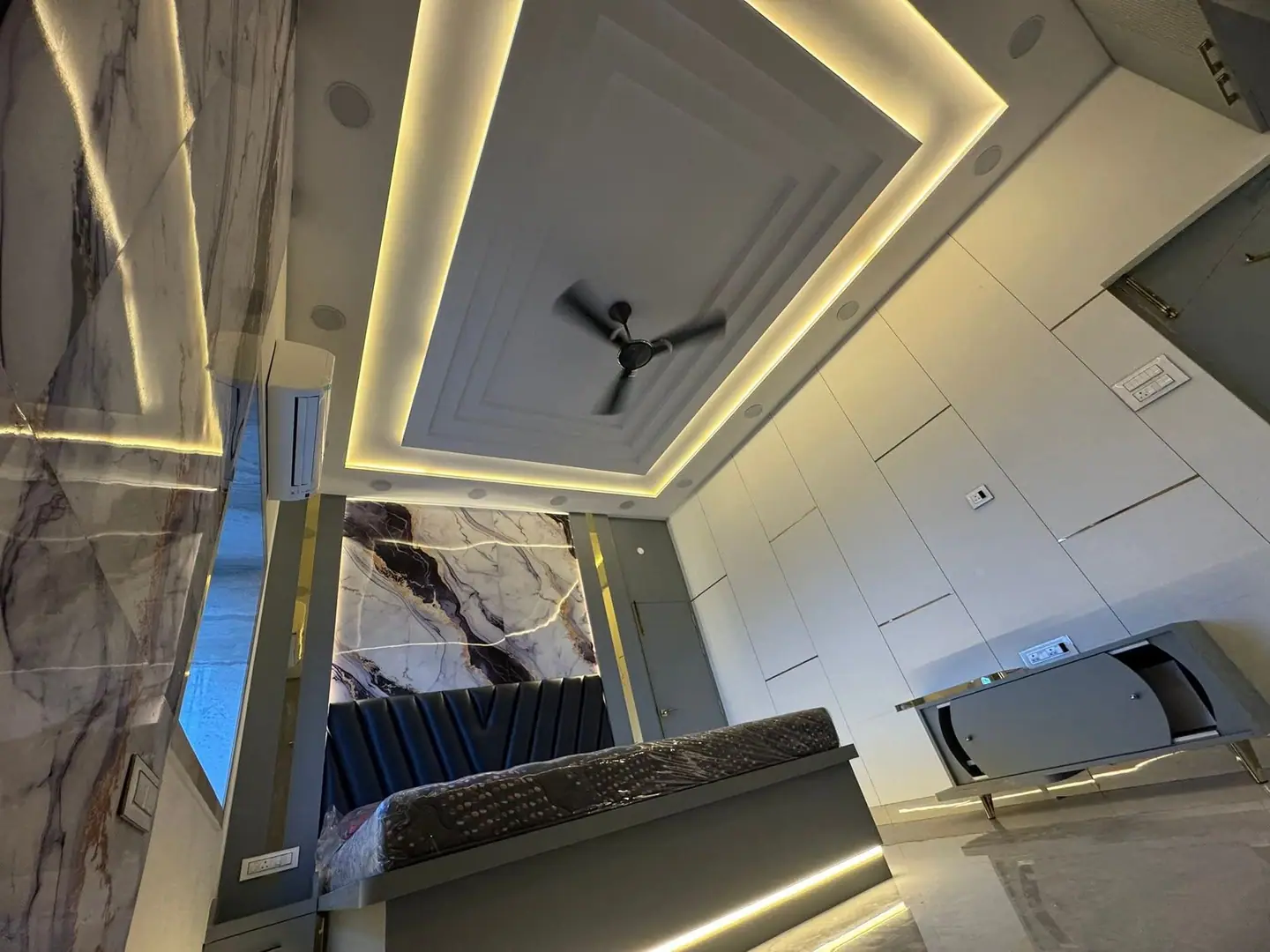 Wide view of a bedroom with a stepped cove ceiling, flush wardrobes and marble-effect walls